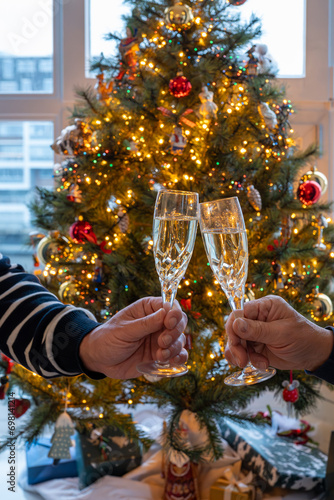 New year or christmas dinner, two man hands with glasses of champagne cava or prosecco wine crystal glasses with christmas tree and garland lights on background