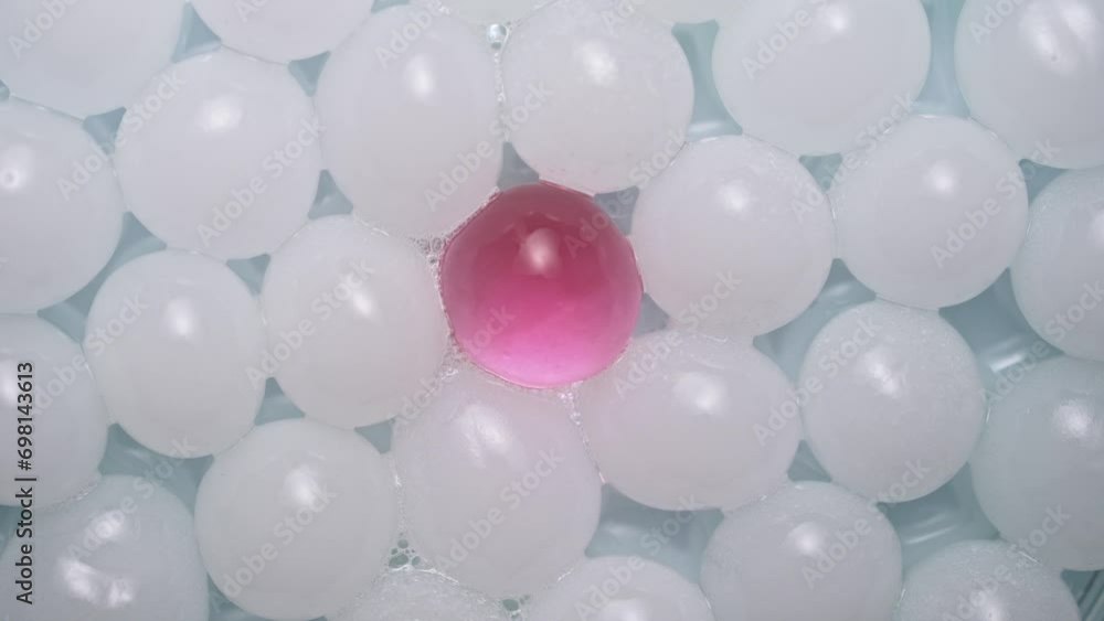 Close up shot of fluid substance on the white background. Cosmetic product gel or serum in white balls pink in the center rotating on the clear surface. Close up shot of fluid substance on the white background. Cosmetic product gel or serum in white balls pink in the center rotating on the clear surface.