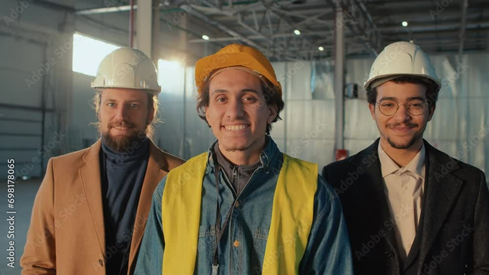 Chest up portrait of happy smiling diverse male business partners and construction engineer in hardhats posing and looking at camera at site indoors Chest up portrait of happy smiling diverse male business partners and construction engineer in hardhats posing and looking at camera at site indoors