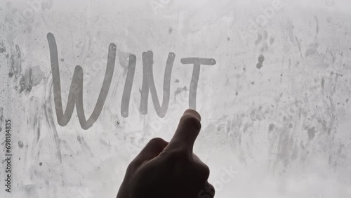 Word Winter drawing with a male finger on glass condensation window by blurred snow-covered background. Handwritten inscription Winter with on a misted window during snowfall. Wintery mood, text. photo