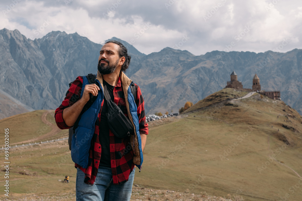 A male tourist on the background of the Trinity Church in Gergeti in the mountains on a clear day.