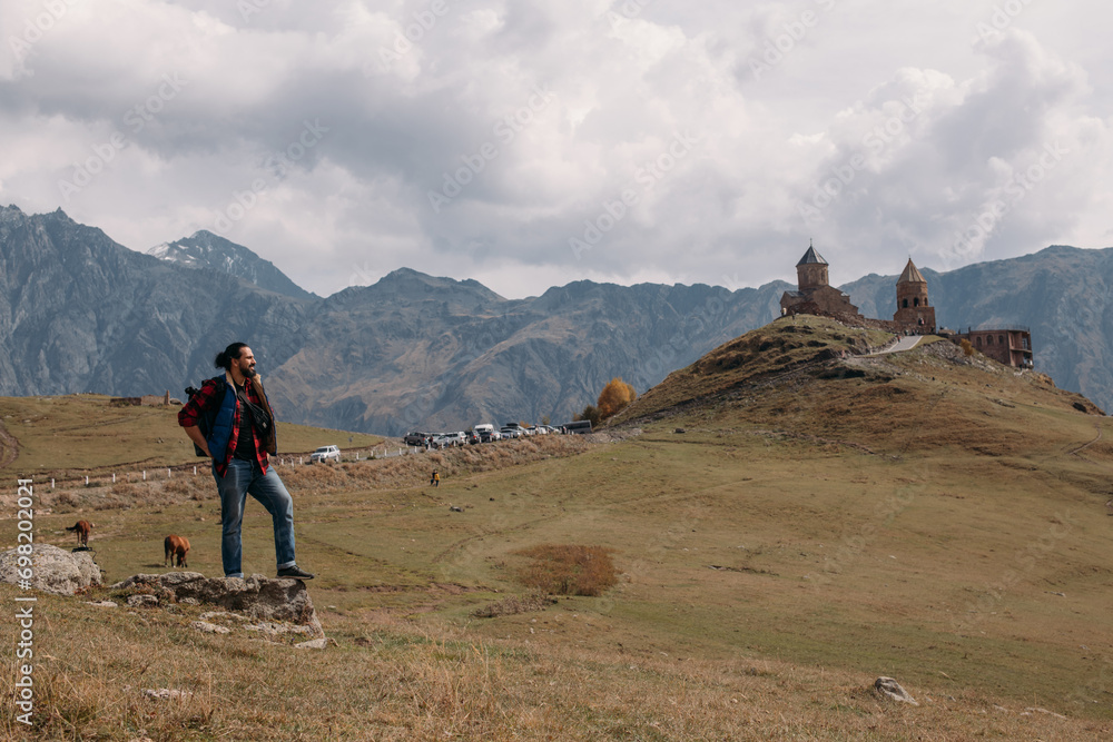 A male tourist on the background of the Trinity Church in Gergeti in the mountains on a clear day.