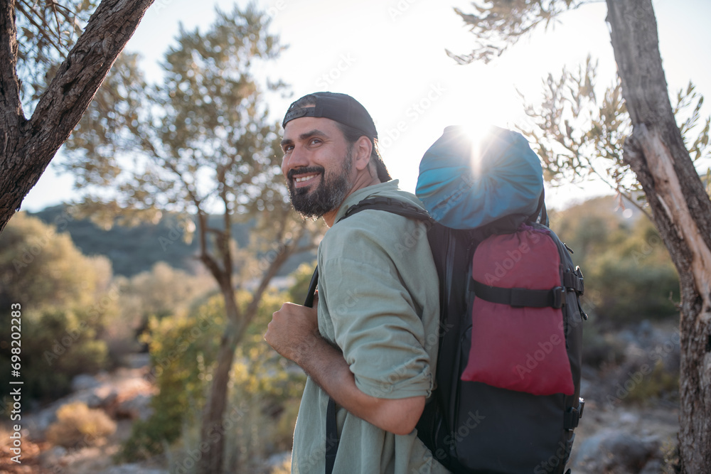 A male tourist with a large backpack and equipment on a mountain trail among the trees.