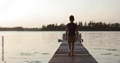 Young boy walking on dock on open ocean looking around nervously photo