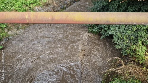 the muddy water moves quickly through the strained riverbed, it is easy to drown, those who fall are swept into the depths under the bridge. the rapid flow of water from field also washes away topsoi photo