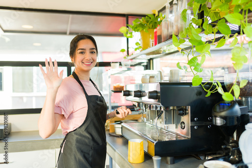 Young woman barista greeting customer in the coffee shop