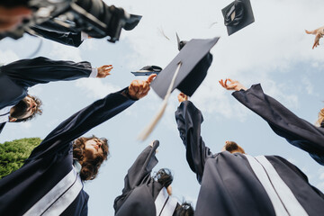 Graduates celebrate in the park wearing gowns, throwing the caps, congratulating each other and having fun after graduation. Last student-life day!