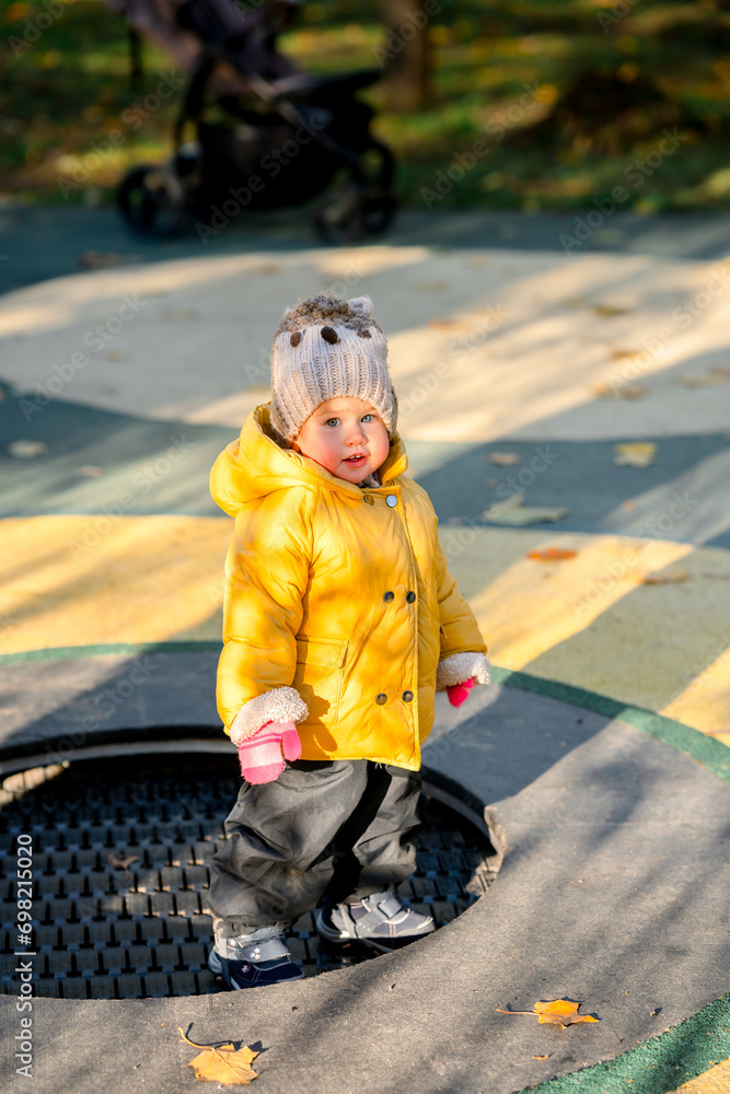 A child toddler in a yellow jacket jumps on a trampoline in the playground in autumn A child toddler in a yellow jacket jumps on a trampoline in the playground in autumn