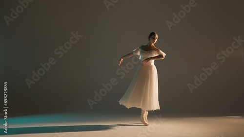 Portrait of female on soft background in warm light in studio. Beautiful ballerina in white tulle showing dance element of choreography.