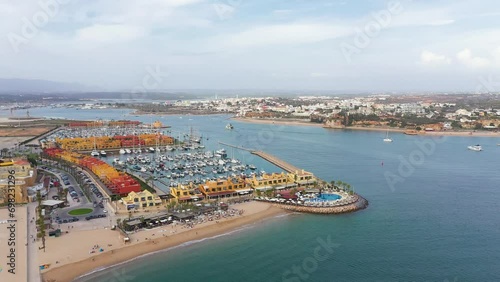 Cinematic aerial perspective of Portimao Marina. Luxury yacht docked in the port. Arade river in the middle. Ferragudo city in background. Drone descending and tilt up. Famous travel destination photo