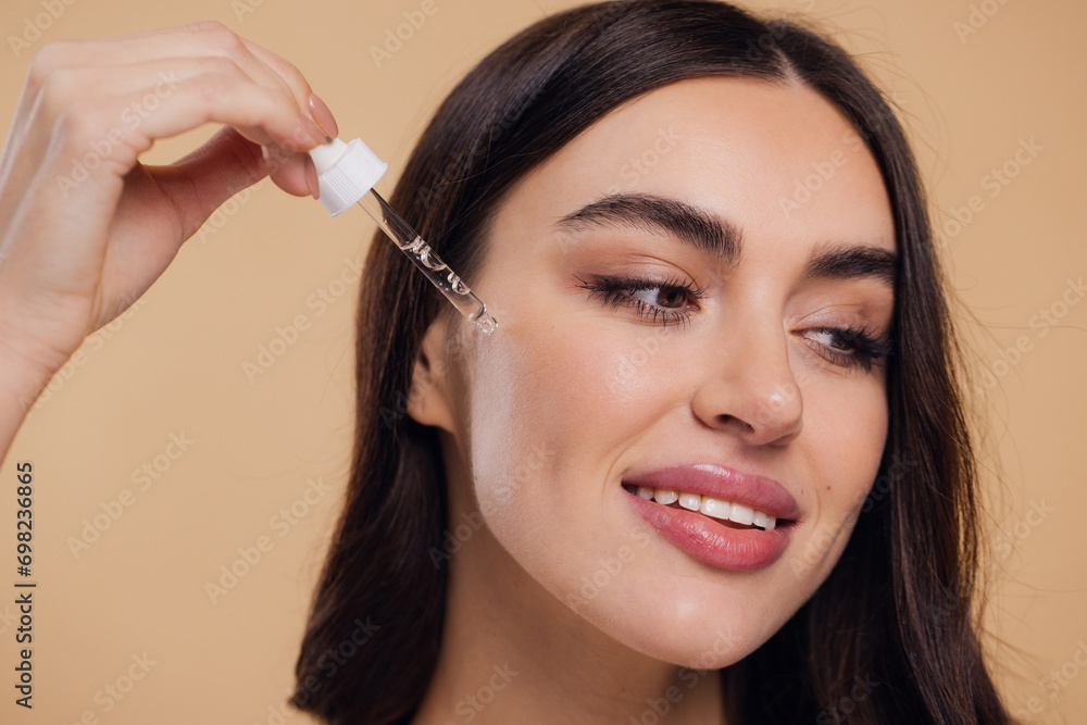 Woman Dropping Serum on Face on Beige Background