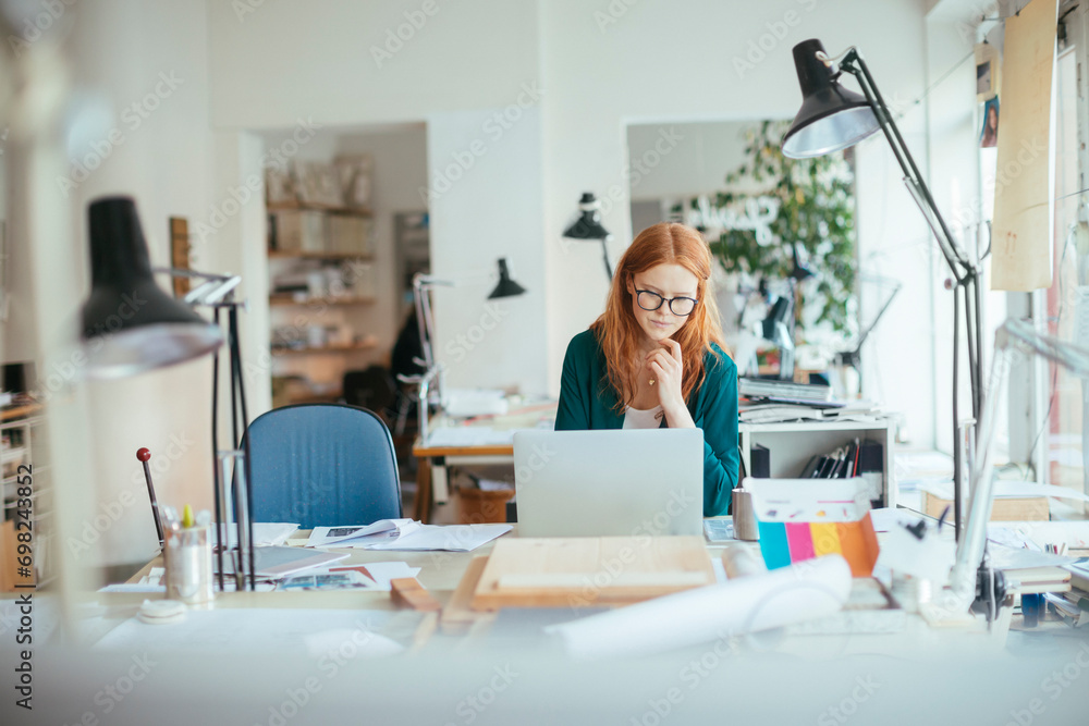 Young female designer working on laptop in office Young female designer working on laptop in office