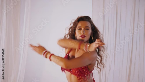 Beautiful girl dances oriental belly dance. Sexy woman in red lingerie is dancing a seductive dance in a white studio. Beautiful stomach and breasts.	
 photo
