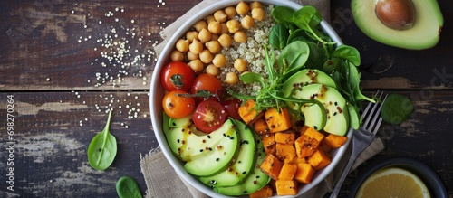 Top view of a vegan lunch bowl containing avocado, quinoa, sweet potato, tomato, spinach, and chickpeas.