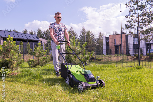 A young woman with a green lawn mower mows the lawn photo