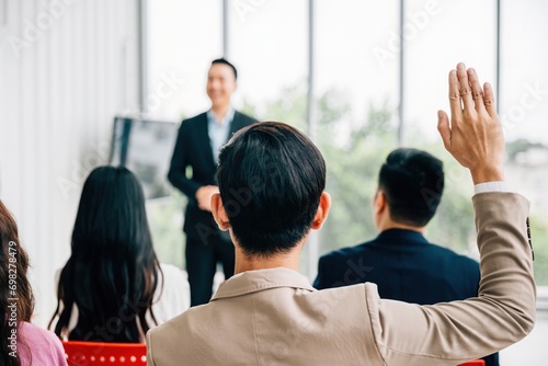 In a conference, hands are raised for questions, reflecting audience engagement and interactive learning. A diverse group participates in a workshop or seminar, fostering teamwork and discussion.