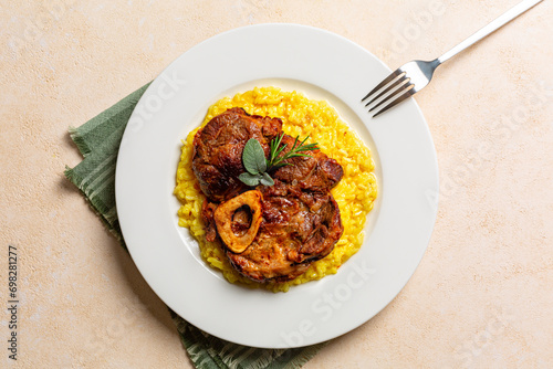Top view of plate with Italian dish Ossobuco, braised beef meat with bone served with saffron risotto alla milanese, specialty of Lombard cuisine. Beige background.