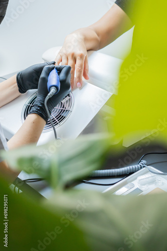 Manicurist uses an electric drill to remove old gel polish from nails. A woman is getting a manicure of nails. The beautician files the client's nails. professional manicure tool. Close-up