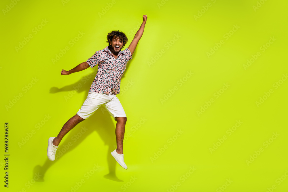 Full size photo of attractive young guy jumping fly raise fist wear trendy pink leopard print outfit isolated on yellow color background