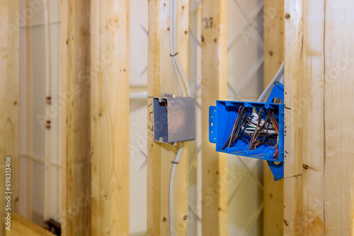 Located on wall above wooden frame beam is plastic electrical switch box with wires