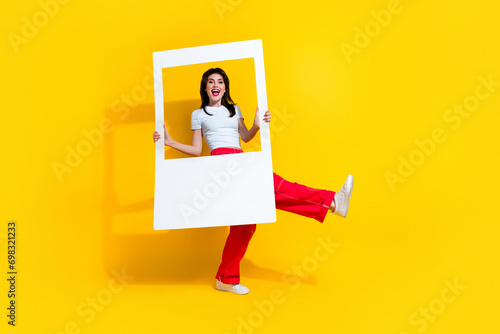 Full length photo of cool impressed woman dressed white t-shirt holding paper photo frame empty space isolated yellow color background