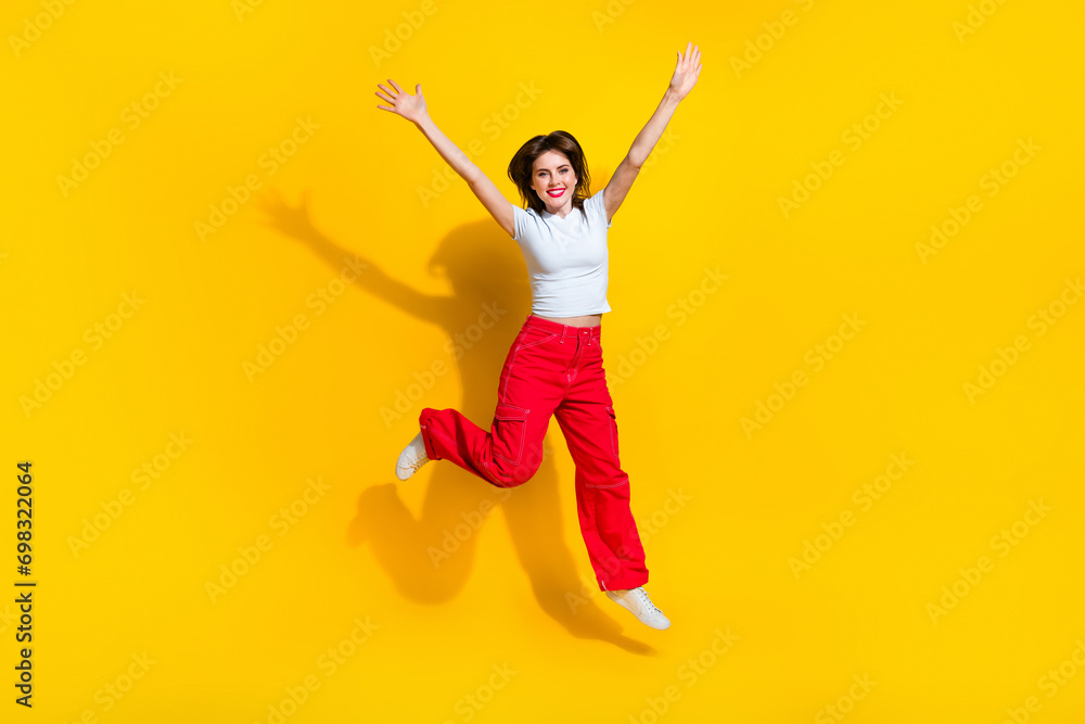 Full length photo of optimistic girl wear t-shirt orange trousers hands up celebrate black friday isolated on yellow color background Full length photo of optimistic girl wear t-shirt orange trousers hands up celebrate black friday isolated on yellow color background