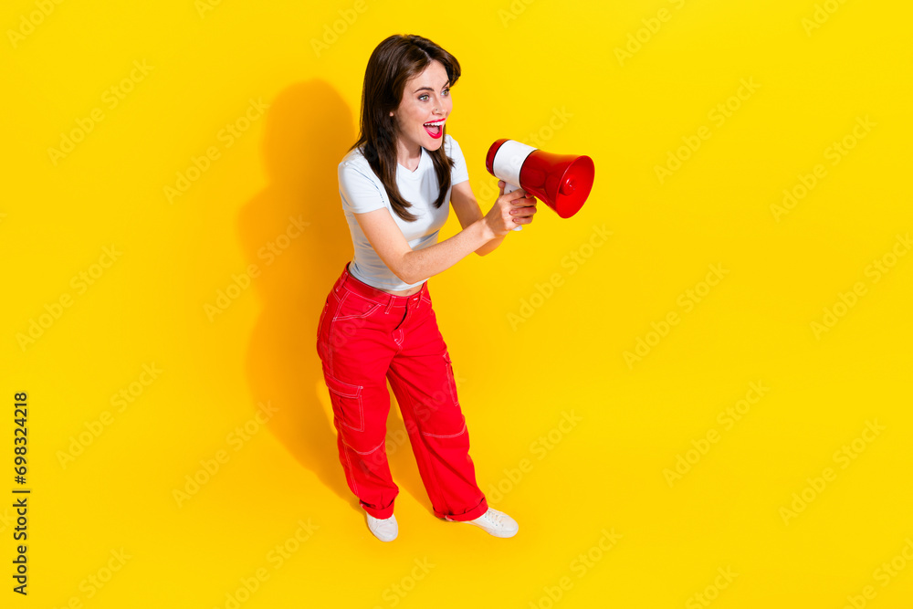 Top view full length photo of excited funky woman dressed white t-shirt scream bullhorn empty space isolated yellow color background Top view full length photo of excited funky woman dressed white t-shirt scream bullhorn empty space isolated yellow color background