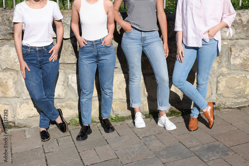 Women in stylish jeans near stone wall outdoors on sunny day, closeup