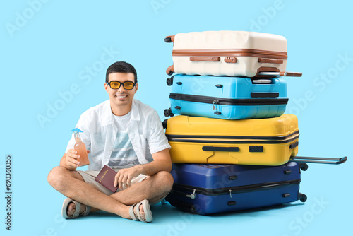 Male tourist with suitcases, passport and lemonade on blue background