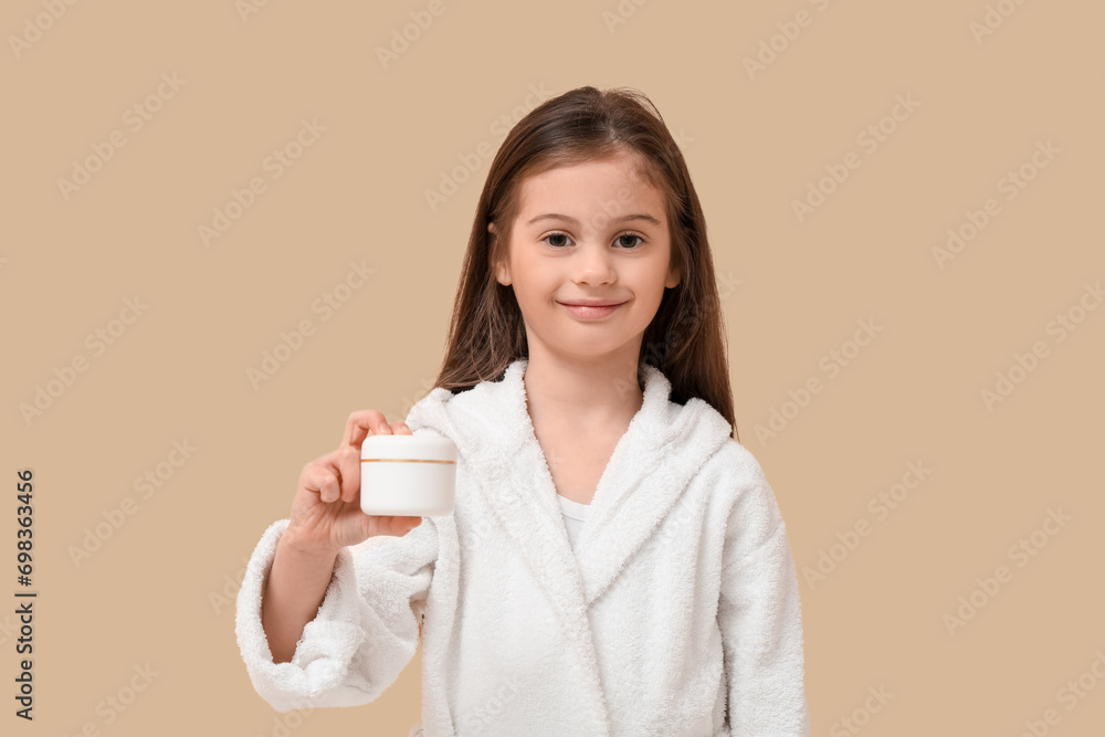 Cute little happy girl in bathrobe with jar of cream on beige background Cute little happy girl in bathrobe with jar of cream on beige background