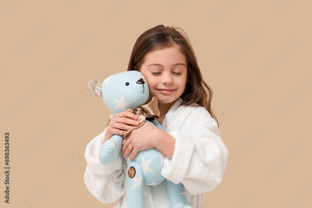 Cute little happy girl in bathrobe with teddy bear on beige background Cute little happy girl in bathrobe with teddy bear on beige background