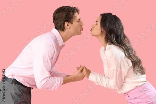 Young couple kissing on pink background. Valentine's Day celebration