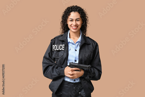 Fotografie Beautiful young happy African-American policewoman with gun on brown background