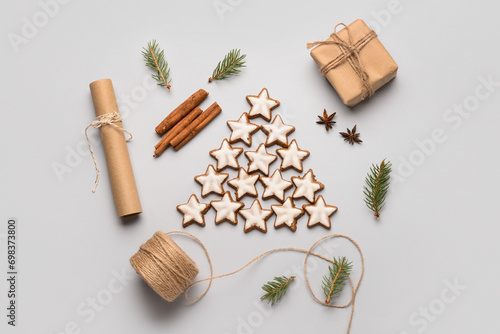 Star-shaped gingerbread cookies with cinnamon, fir branches and gift box on grey background