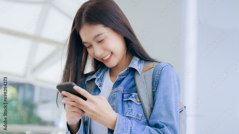 Young asian woman smiling using mobile smart phone outdoor. Happy female tourist wearing jeans jacket and holding smartphone at public Young asian woman smiling using mobile smart phone outdoor. Happy female tourist wearing jeans jacket and holding smartphone at public