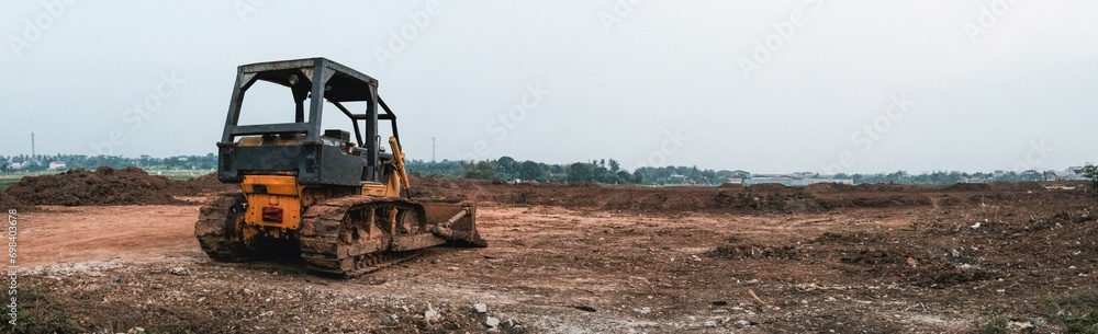 Panoramic view of old rusted metal yellow tractor bulldozer in dry open field.