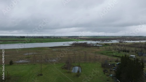 Aerial establishing view of high water in springtime, Alande river (Latvia) flood, brown and muddy water, agricultural fields under the water, overcast day, wide drone shot moving forward photo