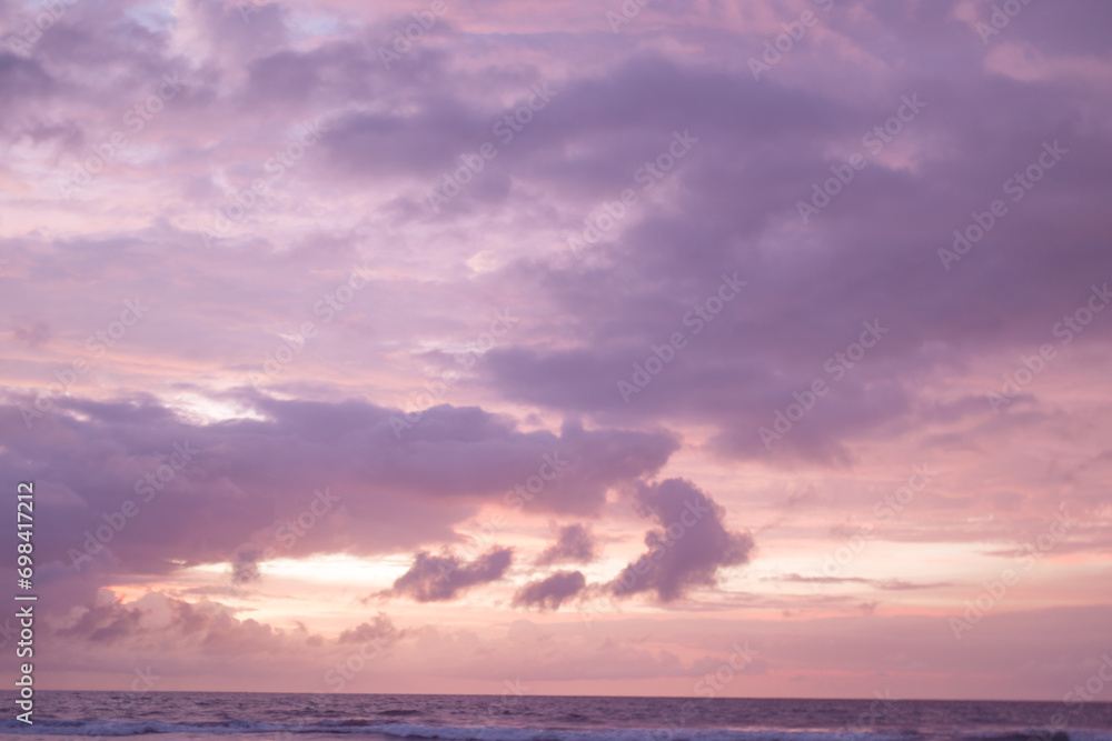 Orange sun and lilac clouds on the background of the ocean. Beautiful sunset on the beach