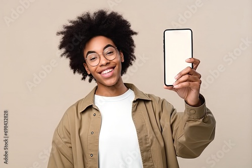 happy african american teen student holding mobile cell phone pointing finger smartphone mock big screen template presenting application using cellphone showing ad isolated beige background photo