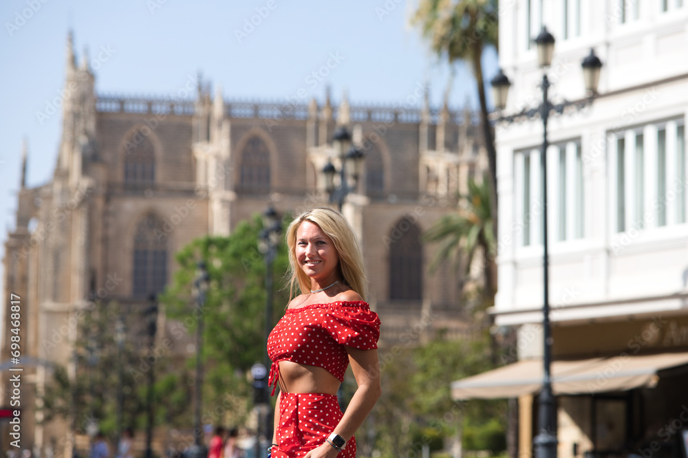 Fototapeta premium Young and beautiful blonde woman from the United States is on a sightseeing trip to Seville, Spain. The woman is enjoying her holidays in europe. She is between the rails of the urban tram.