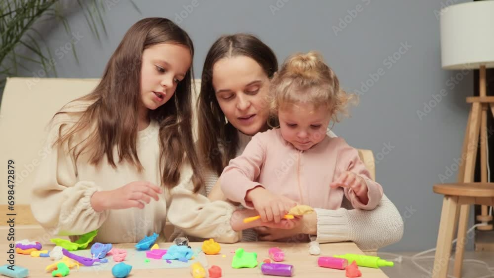 Dark haired Caucasian woman teaching kids handcraft at kindergarten or playschool playing together with colorful plasticine calming down crying infant baby Dark haired Caucasian woman teaching kids handcraft at kindergarten or playschool playing together with colorful plasticine calming down crying infant baby