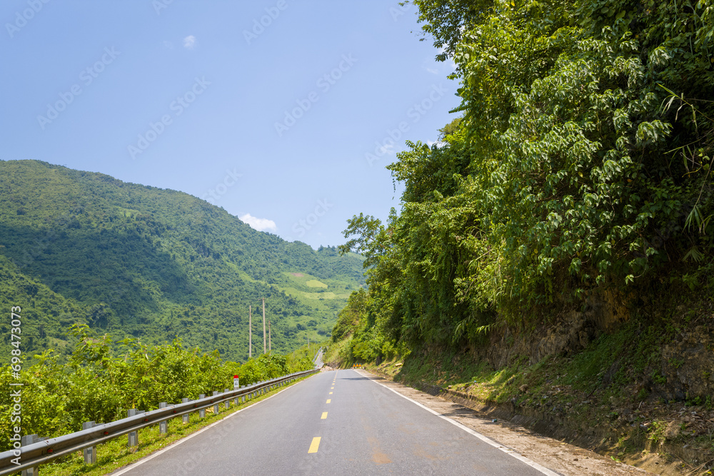An asphalt road in the middle of the countryside and mountains, in Asia, Vietnam, Tonkin, between Dien Bien Phu and Lai Chau, in summer, on a sunny day.