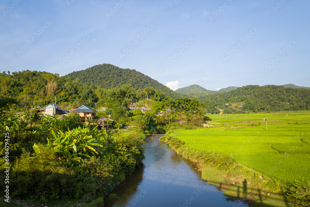 A river at the foot of a village on the edge of rice fields and mountains, in Asia, Vietnam, Tonkin, between Son La and Dien Bien Phu, in summer, on a sunny day.