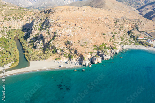 The sandy beach at the foot of the mountain next to a green palm grove , in Europe, Greece, Crete, Preveli, By the Mediterranean Sea, in summer, on a sunny day.