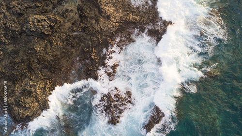 Drone view of Atlantic ocean waves meet with underwater pointed rocky. Blue rough sea with big waves with foam crashing against the rocks, south of Tenerife, Canary island