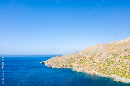 The arid rocky coast and its green countryside along small beaches, in Europe, Greece, Crete, towards Preveli, At the edge of the Mediterranean Sea, in summer, on a sunny day.