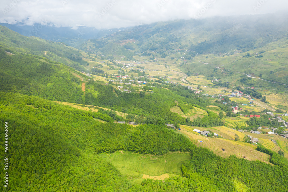 The traditional village on the mountainsides with tropical forests with green and yellow rice terraces, in Asia, Vietnam, Tonkin, Sapa, towards Lao Cai, in summer, on a cloudy day.