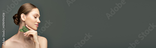 young woman doing face massage with jade gua sha stone on grey background, facial care banner photo