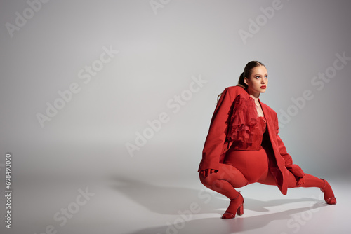 high fashion model in stylish red outfit with tights and high heels posing on grey background photo