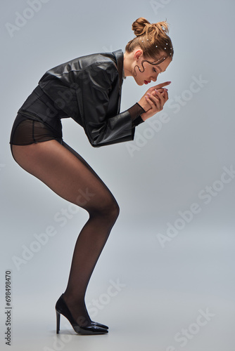 side view of trendy model in pearl hair pins posing in black tights and high heels on grey backdrop